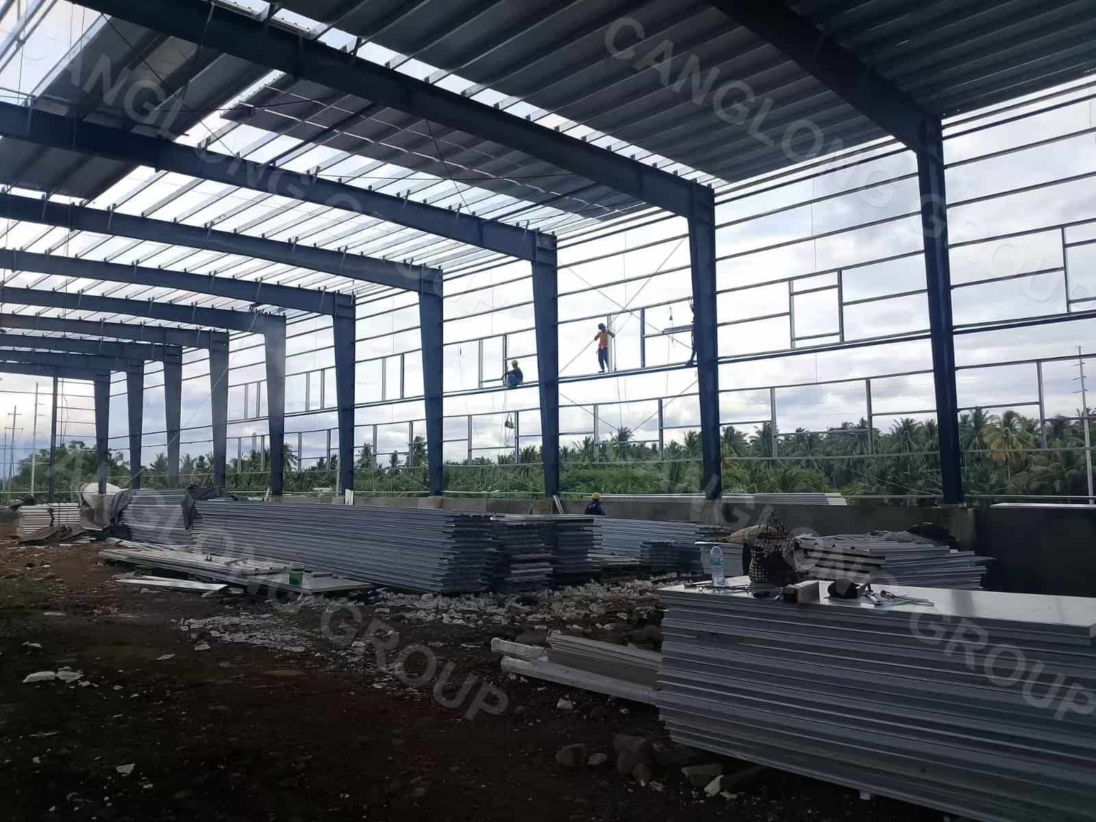 Portal frame columns and rafters of a 36 m span food factory steel warehouse under erection in Davao, Philippines, with EPS sandwich panels staged on the slab