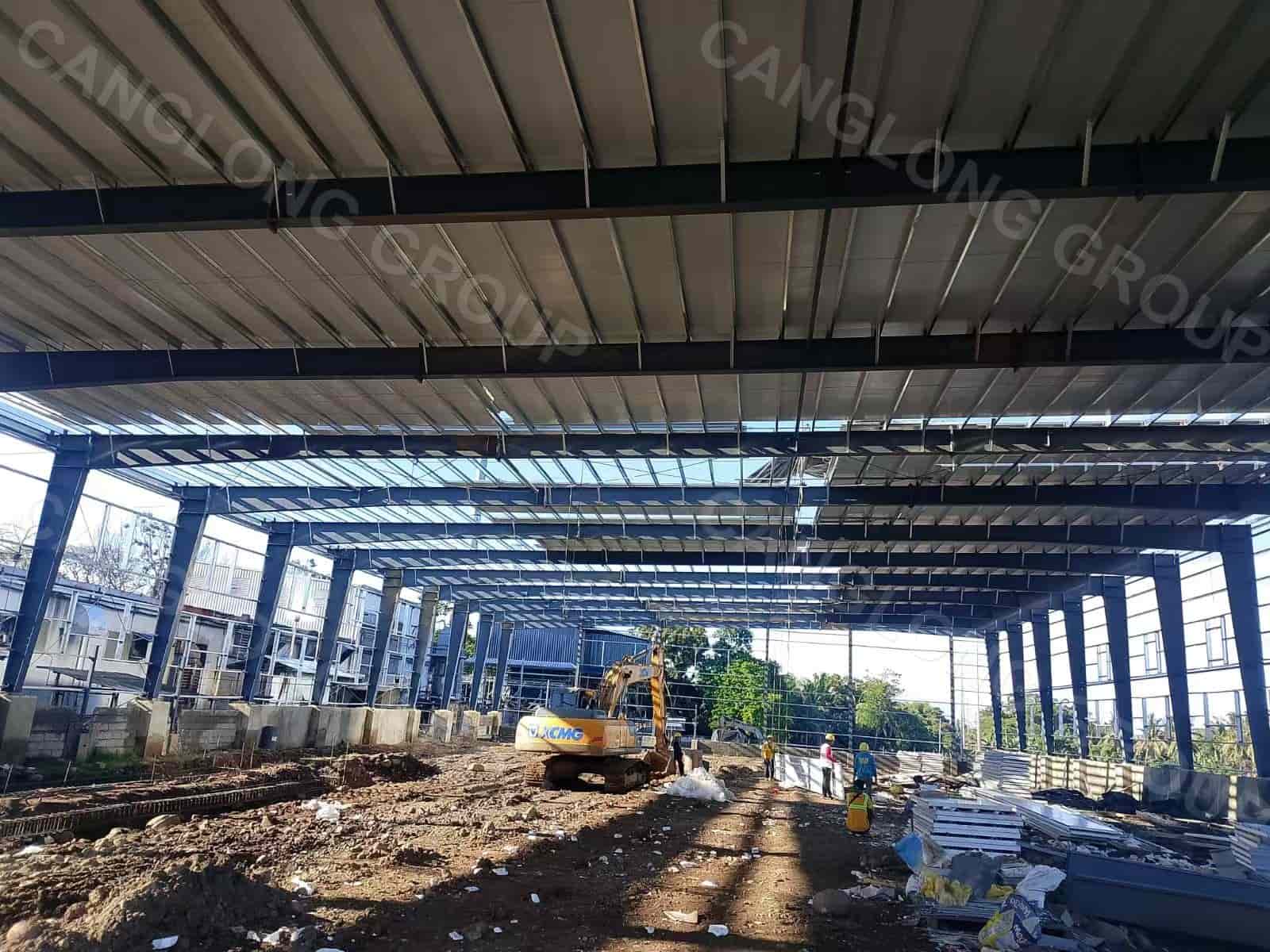 Interior view of the 36 m clear span portal frame warehouse in Davao during roof sheeting, showing the column-free floor of the food factory building