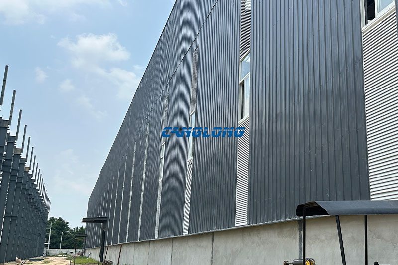 Electric roller shutter door at the Bangkok plant entrance seen from inside, with steel louvre windows and aluminium sliding windows on the gable wall above