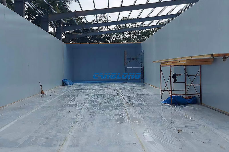 Interior aisle of the Cebu cold room shed between white panel cold room boxes, with the insulated roof structure and purlins open above