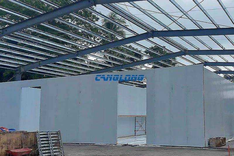 White PU panel cold room boxes standing inside the open steel shed in Cebu, with the insulated roof structure visible above and door openings cut into the panels
